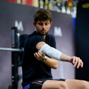 Man wearing the white ELBOW Support Premier Padel brace after training